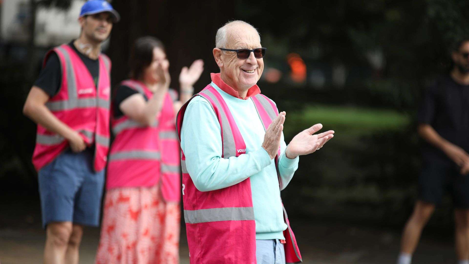 Older man with pink vest and sun glasses applauding and smiling