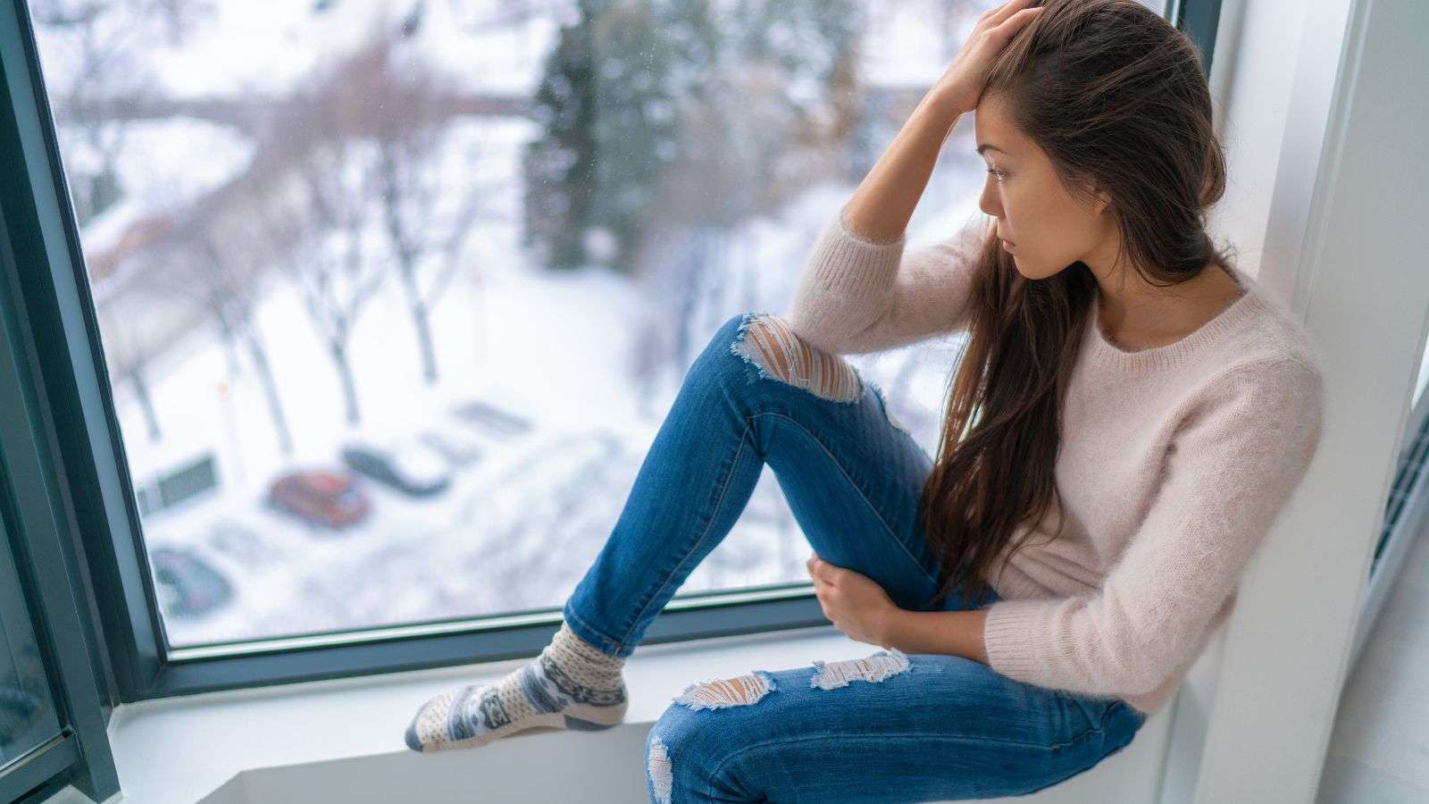 woman looking out of the window in winter with a sad expression on her face