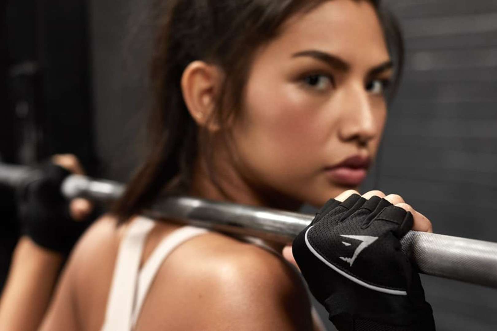 A woman lifts weights while wearing lifting gloves.