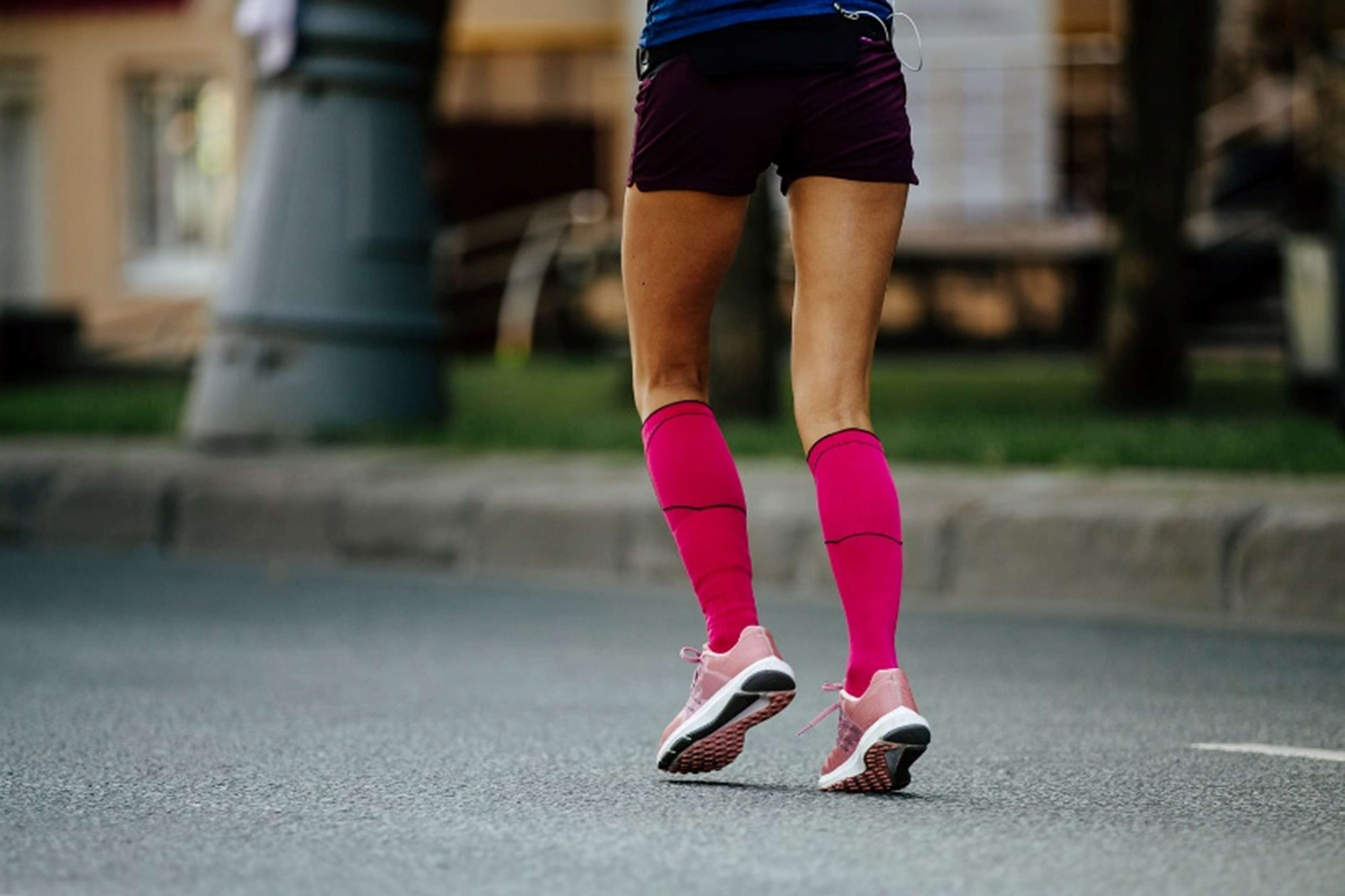 Runner wearing bright pink compression socks and athletic shoes running on a city street, highlighting protection for feet prone to blisters during activity.